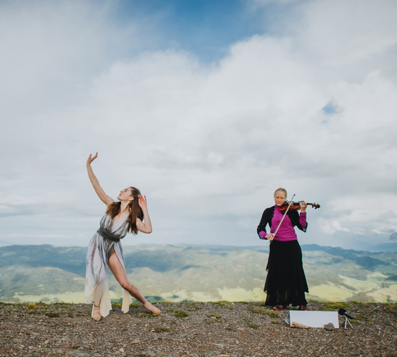 Two women playing violin on top of a mountain.