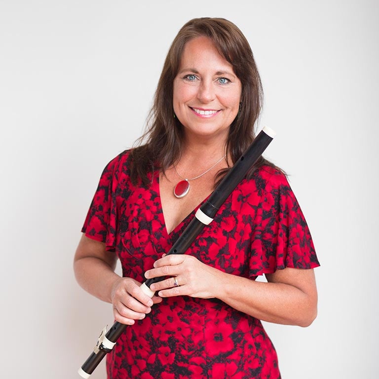 Kathie Steward in a red patterned dress holds a flute, smiling in front of a plain background.