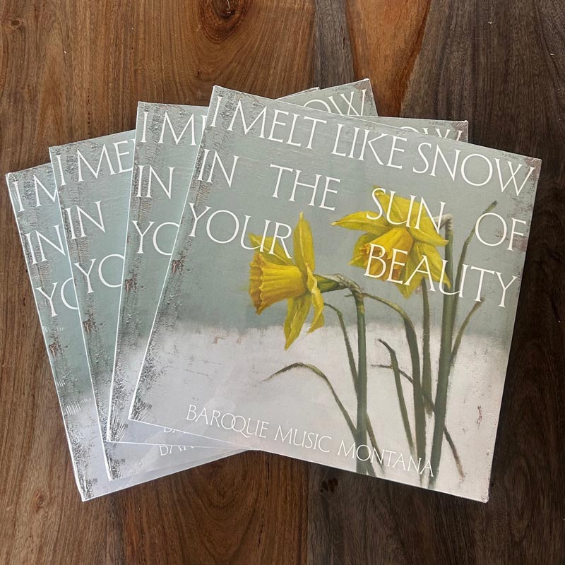 Four Baroque Music Montana albums with cover art of yellow daffodils and the text “I Melt Like Snow in the Sun of Your Beauty” stacked on a wooden surface.